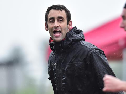 马特·科恩(Matt Cohen)穿着黑色雨衣，向男子越野队的一名队员大喊指令.