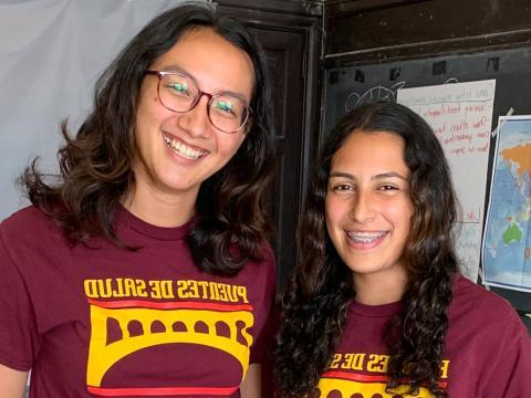 24岁的Sunny Martinez站在黑板前, 22岁的Keishla Sanchez和24岁的Elana Bien站在Puentes de Salud的教室里.