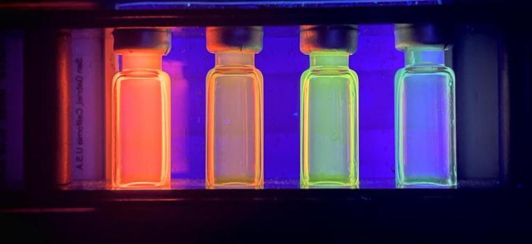 图中显示了四个装有量子点的小瓶吸收紫外线并在不同波长重新发射光, 是什么产生了鲜艳的颜色. 伊森·贝克'24，第一名冠军，2022年KINSC科学成像比赛.
